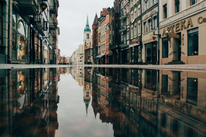 A tranquil street in Toruń, Poland, with historic architecture reflecting in a puddle.