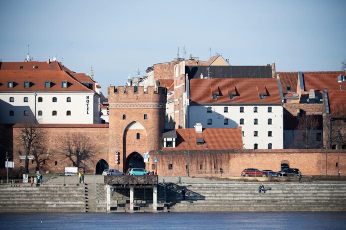 Toruń's medieval city gate by the riverside, showcasing red-brick architecture and urban charm.